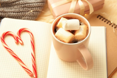 Photo of Hot winter drink in cup and candy canes on notebooks. Cozy season