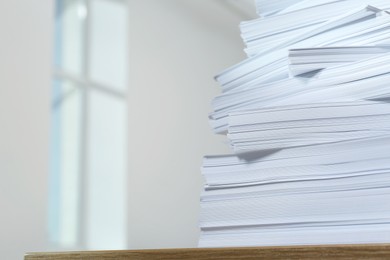 Stack of paper sheets on wooden table against blurred background, closeup. Space for text