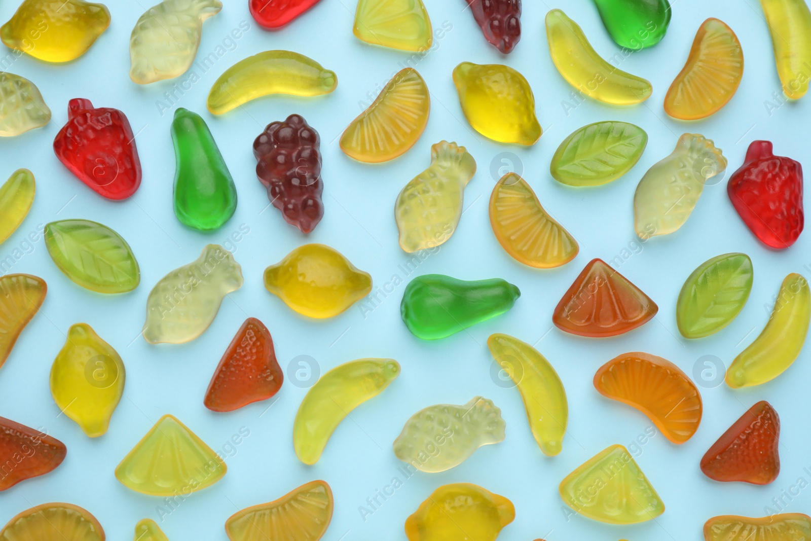 Photo of Tasty jelly candies in shape of different fruits on light blue background, flat lay