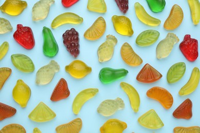 Tasty jelly candies in shape of different fruits on light blue background, flat lay