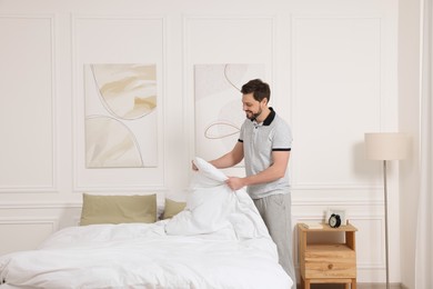 Photo of Man changing bed linens at home. Space for text