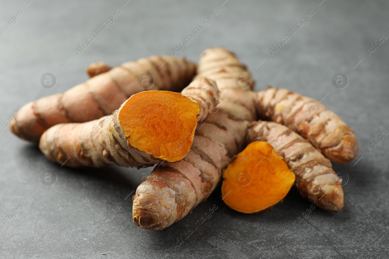 Photo of Whole and cut turmeric roots on grey table, closeup