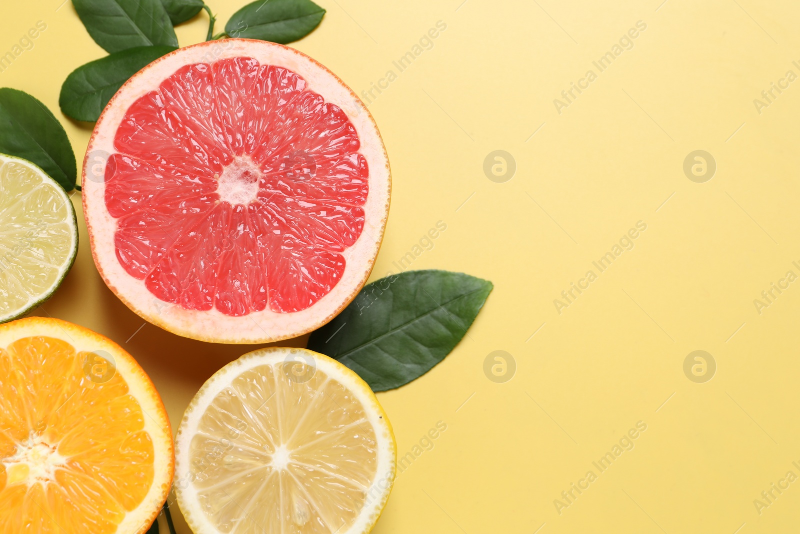 Photo of Different cut citrus fruits and leaves on yellow table, flat lay. Space for text