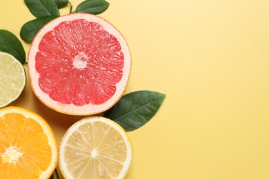 Different cut citrus fruits and leaves on yellow table, flat lay. Space for text