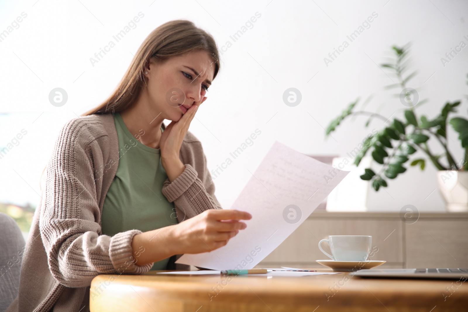 Photo of Worried woman reading letter at wooden table in room