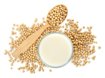 Glass of fresh soy milk and spoon with beans on white background, top view