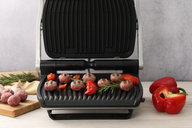 Photo of Electric grill with vegetables, meat balls and rosemary on wooden table