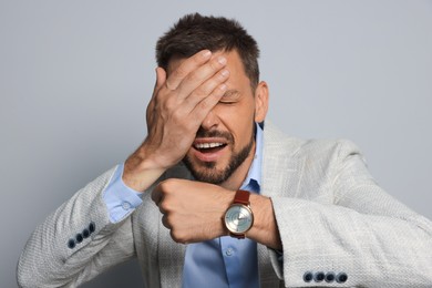 Emotional man showing time on watch against grey background. Being late concept
