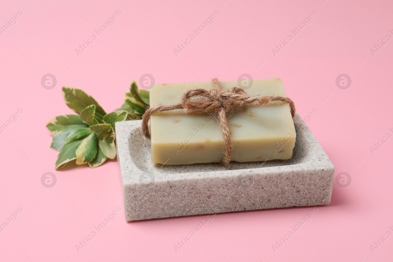 Photo of Dish with soap bar and plant branch on pink background