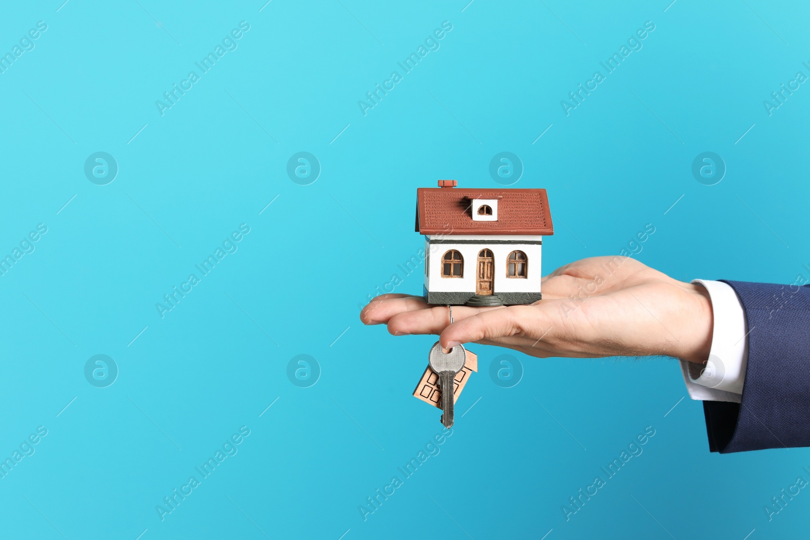 Photo of Real estate agent holding house model and key on color background, closeup