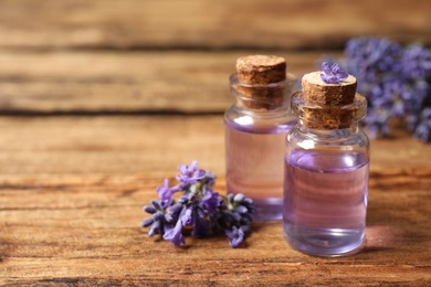 Photo of Bottles of essential oil and lavender flowers on wooden table. Space for text