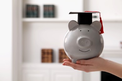 Photo of Woman holding piggy bank and graduation cap indoors, closeup with space for text. Scholarship concept