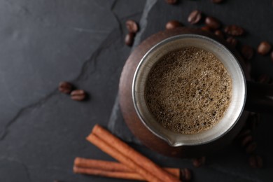 Cezve with Turkish coffee, beans and cinnamon on dark grey table, flat lay. Space for text