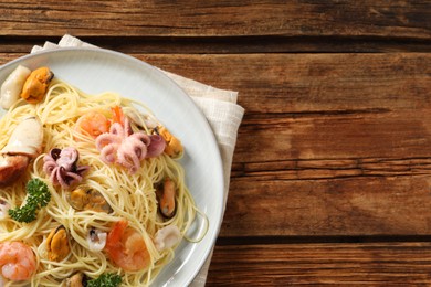 Photo of Delicious spaghetti with seafood served on wooden table, top view. Space for text