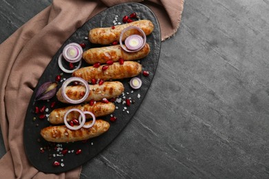 Photo of Tasty grilled sausages with onion rings and pomegranate seeds served on grey table, top view. Space for text