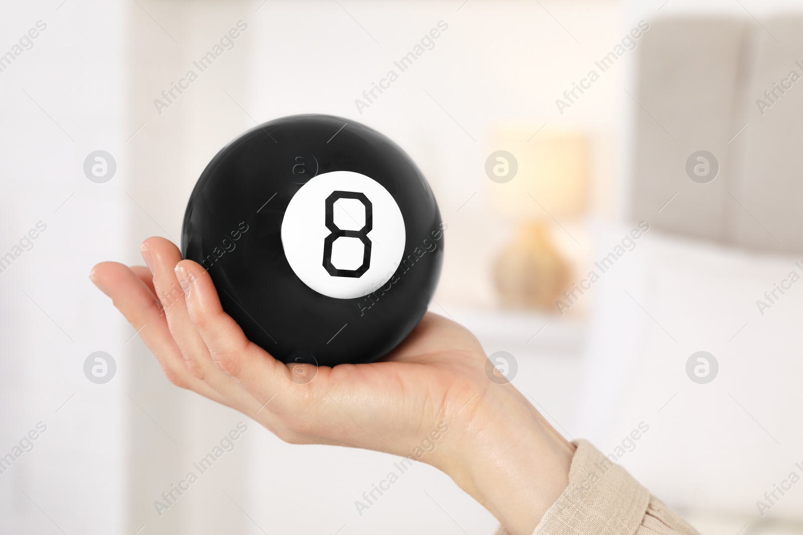 Photo of Woman holding magic eight ball indoors, closeup