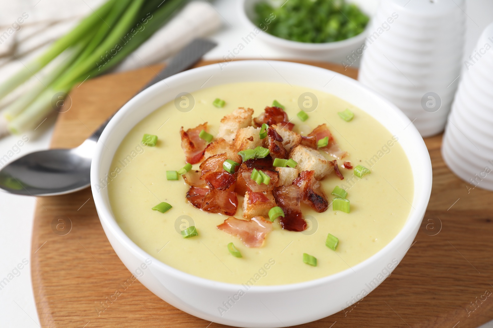 Photo of Tasty potato soup with bacon in bowl and spoon on white table, closeup