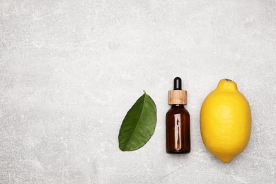 Bottle of essential oil with lemon and leaf on grey table, flat lay. Space for text