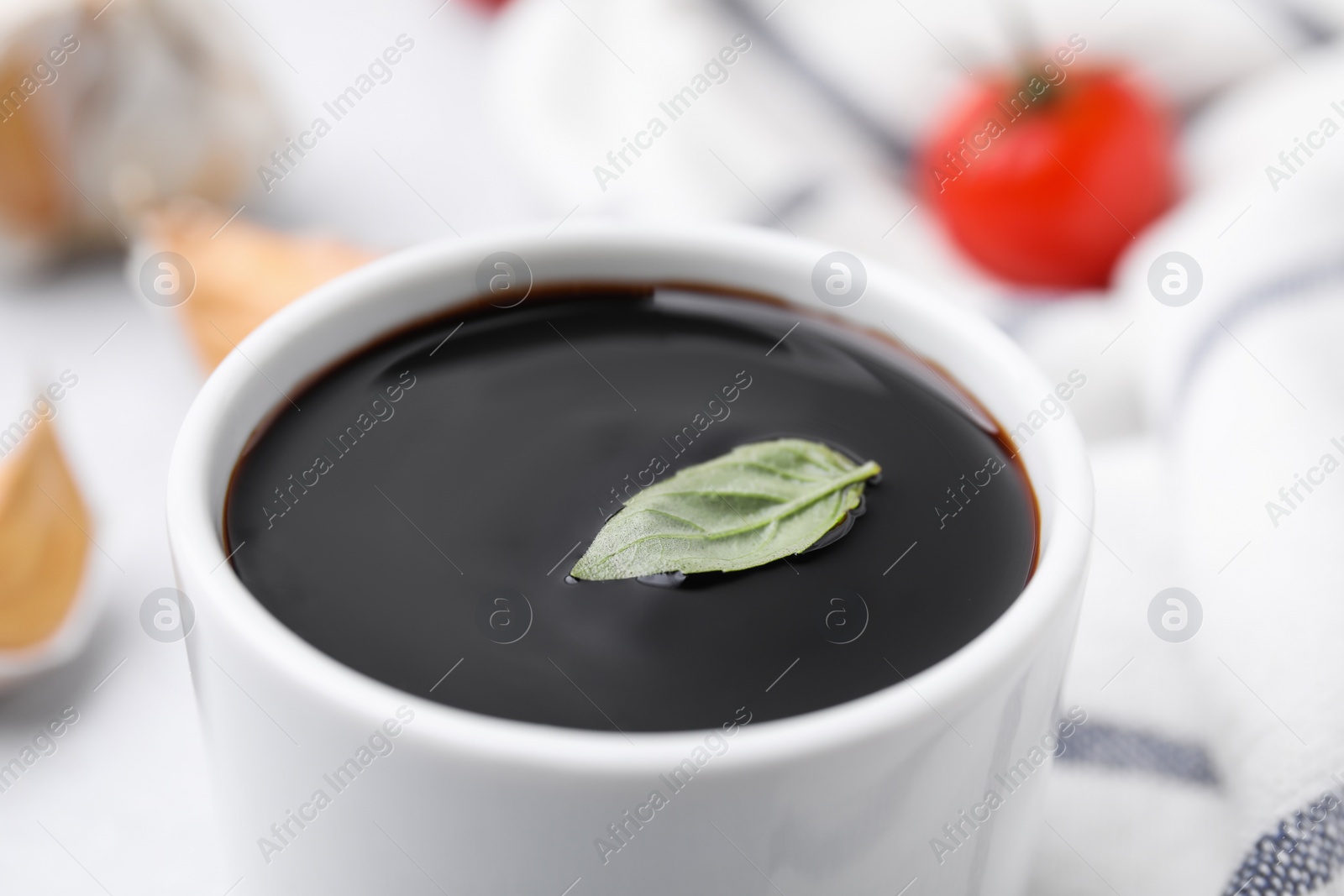 Photo of Organic balsamic vinegar with basil leaf in bowl, closeup