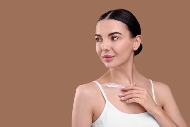 Photo of Beautiful woman with smear of body cream on her collarbone against light brown background. Space for text