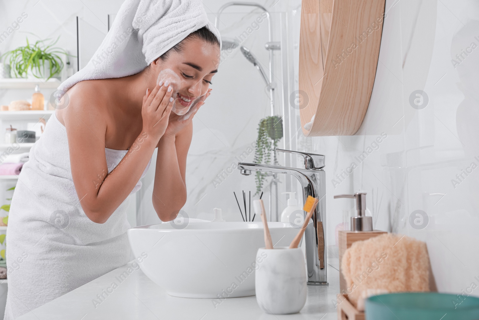 Photo of Beautiful young woman applying cleansing foam onto face in bathroom. Skin care cosmetic