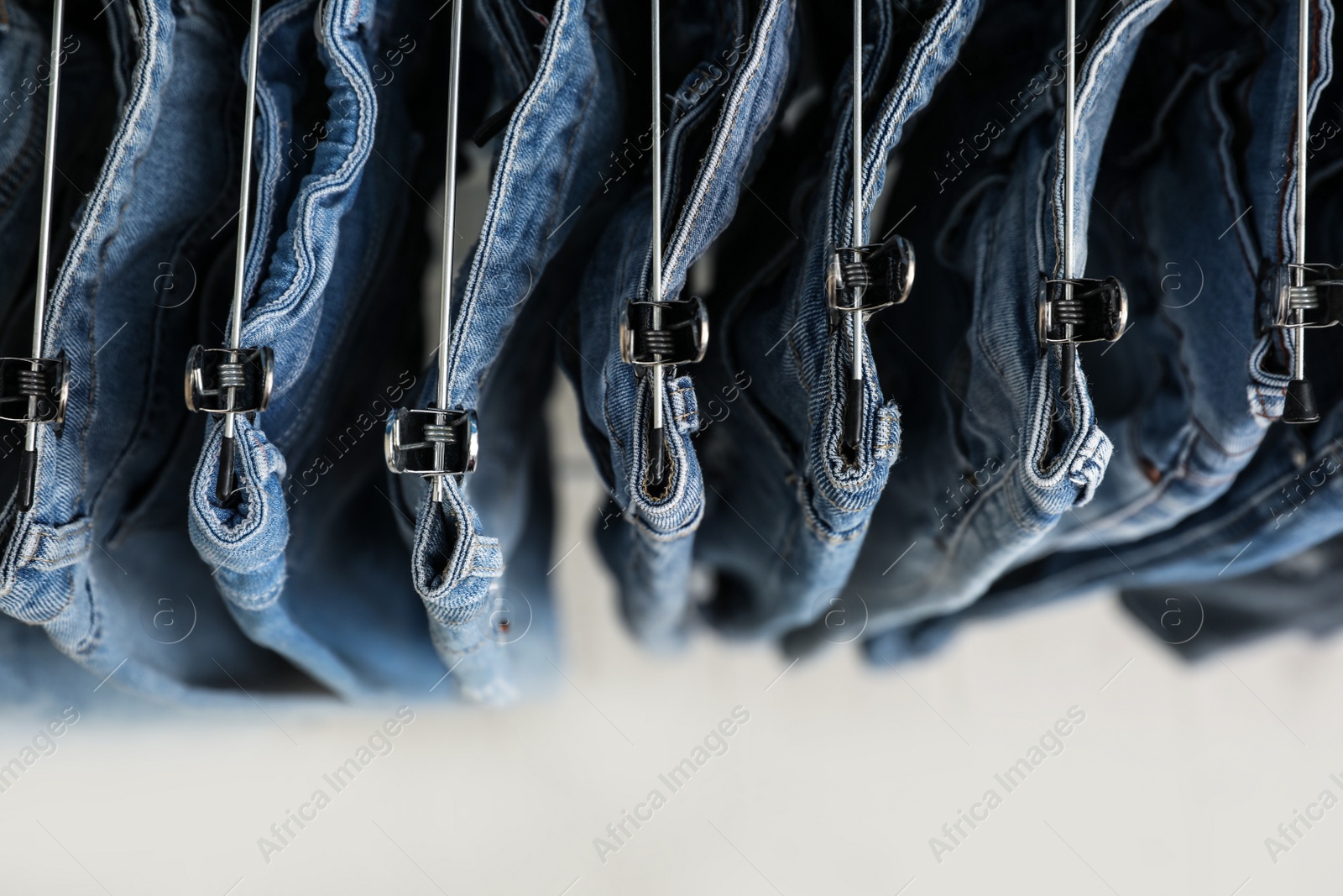 Photo of Top view of hangers with stylish jeans on light background, closeup