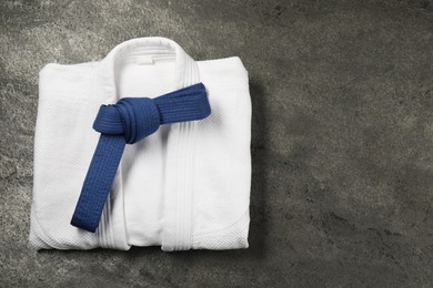 Photo of Blue karate belt and white kimono on gray textured background, top view. Space for text