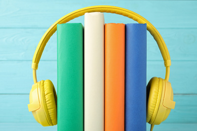 Books and modern headphones on light blue wooden background, closeup