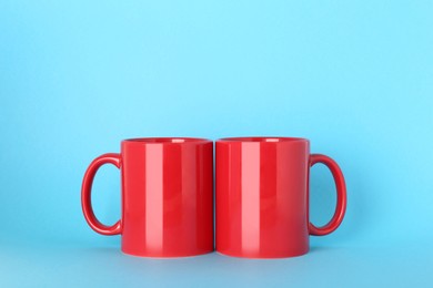 Photo of Blank red ceramic mugs on light blue background