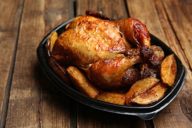 Photo of Delicious grilled whole chicken with potato in plastic container on wooden table. Food delivery service