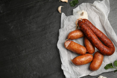 Delicious smoked sausages with garlic on black table, flat lay. Space for text