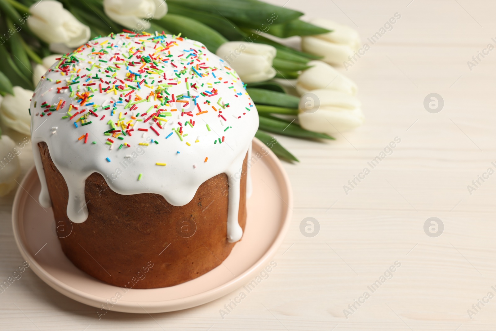 Photo of Delicious Easter cake with sprinkles and beautiful tulips on white wooden table. Space for text