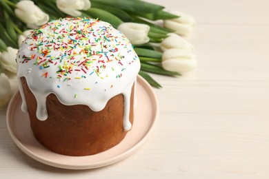 Delicious Easter cake with sprinkles and beautiful tulips on white wooden table. Space for text