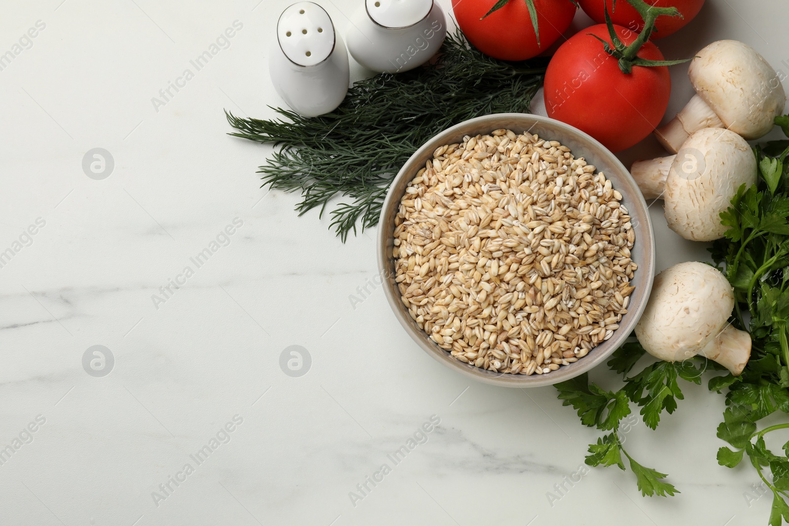 Photo of Dry pearl barley in bowl and products on white marble table, flat lay. Space for text