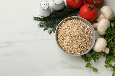 Photo of Dry pearl barley in bowl and products on white marble table, flat lay. Space for text