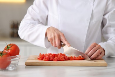 Professional chef cutting tomatoes at white marble table indoors, closeup