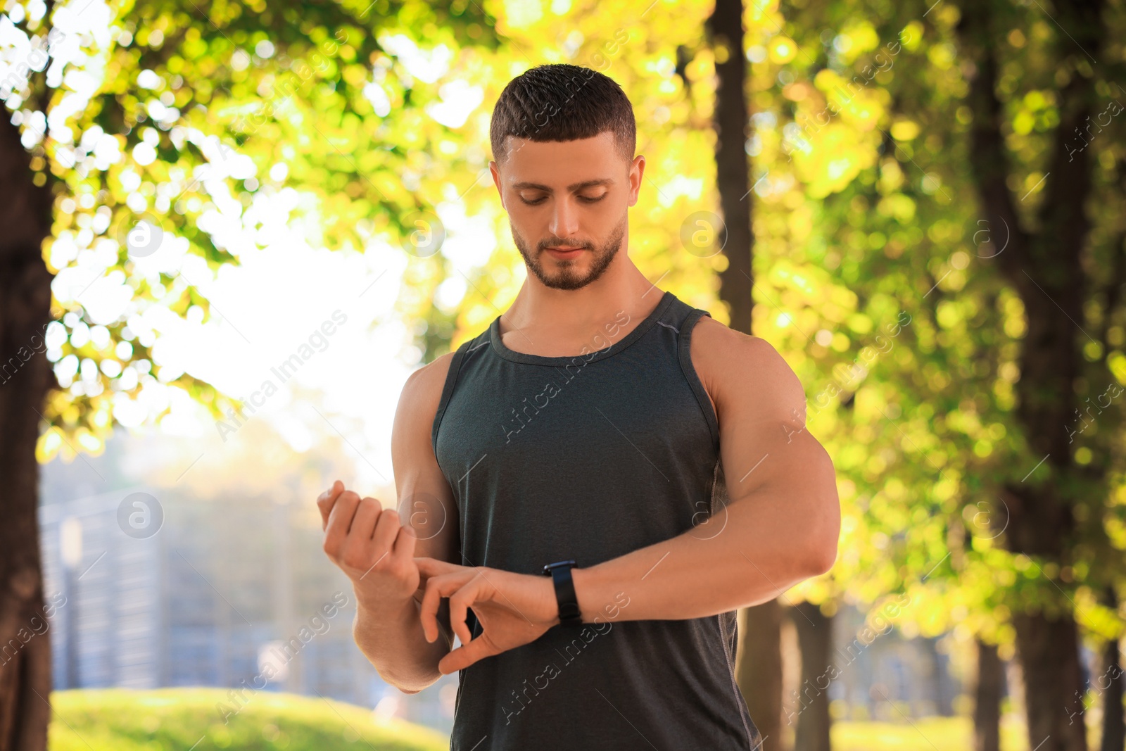 Photo of Attractive serious man checking pulse after training in park on sunny day