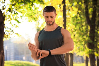 Photo of Attractive serious man checking pulse after training in park on sunny day