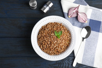 Photo of Flat lay composition with bowl of buckwheat porridge served on dark table