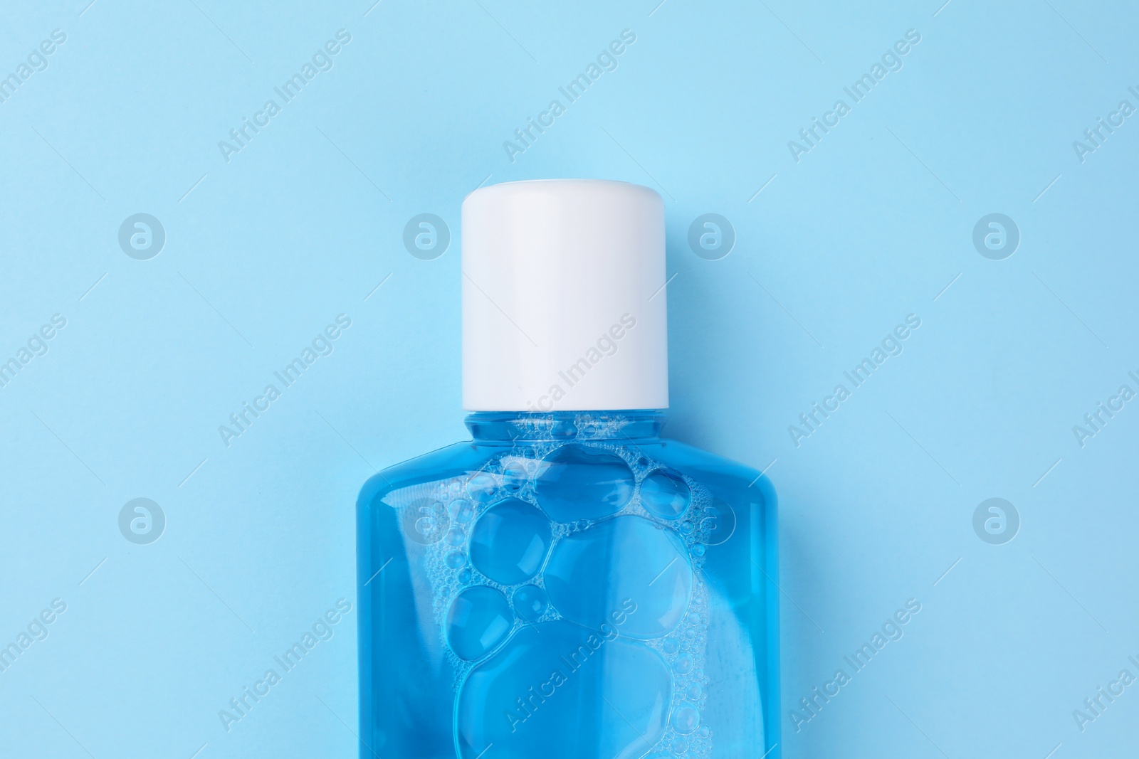 Photo of Fresh mouthwash in bottle on light blue background, top view