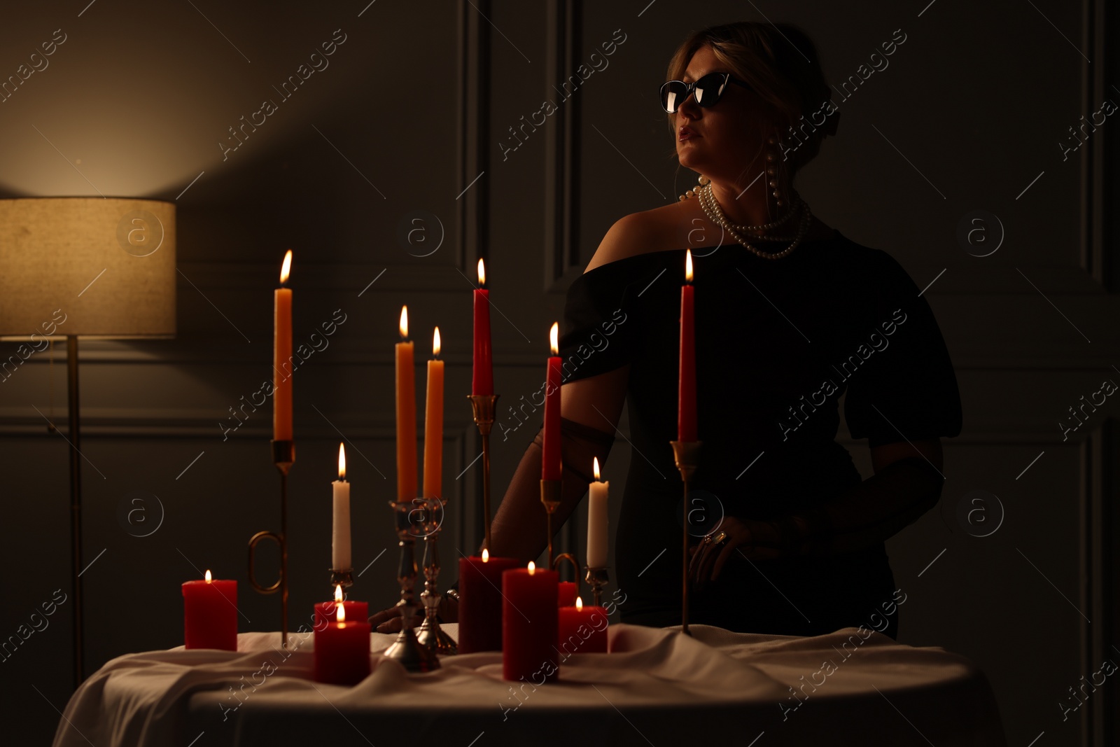 Photo of Beautiful young woman in sunglasses near table with burning candles at night