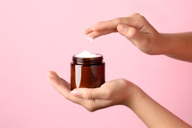 Photo of Woman with jar of face cream on pale pink background, closeup