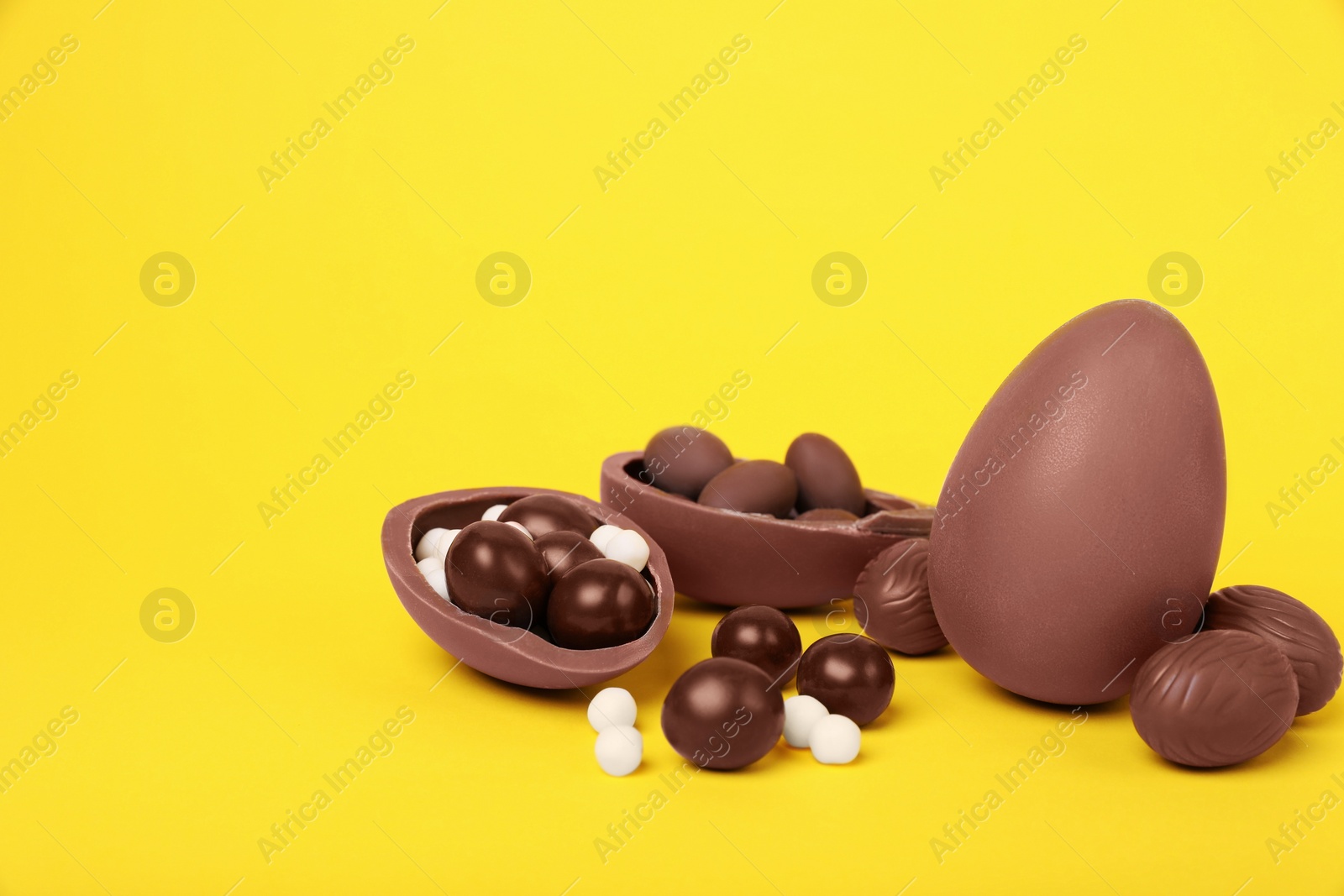 Photo of Delicious chocolate eggs and candies on yellow background. Space for text