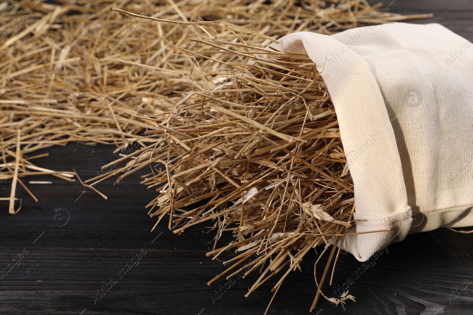 Photo of Dried straw in burlap sack on dark wooden table