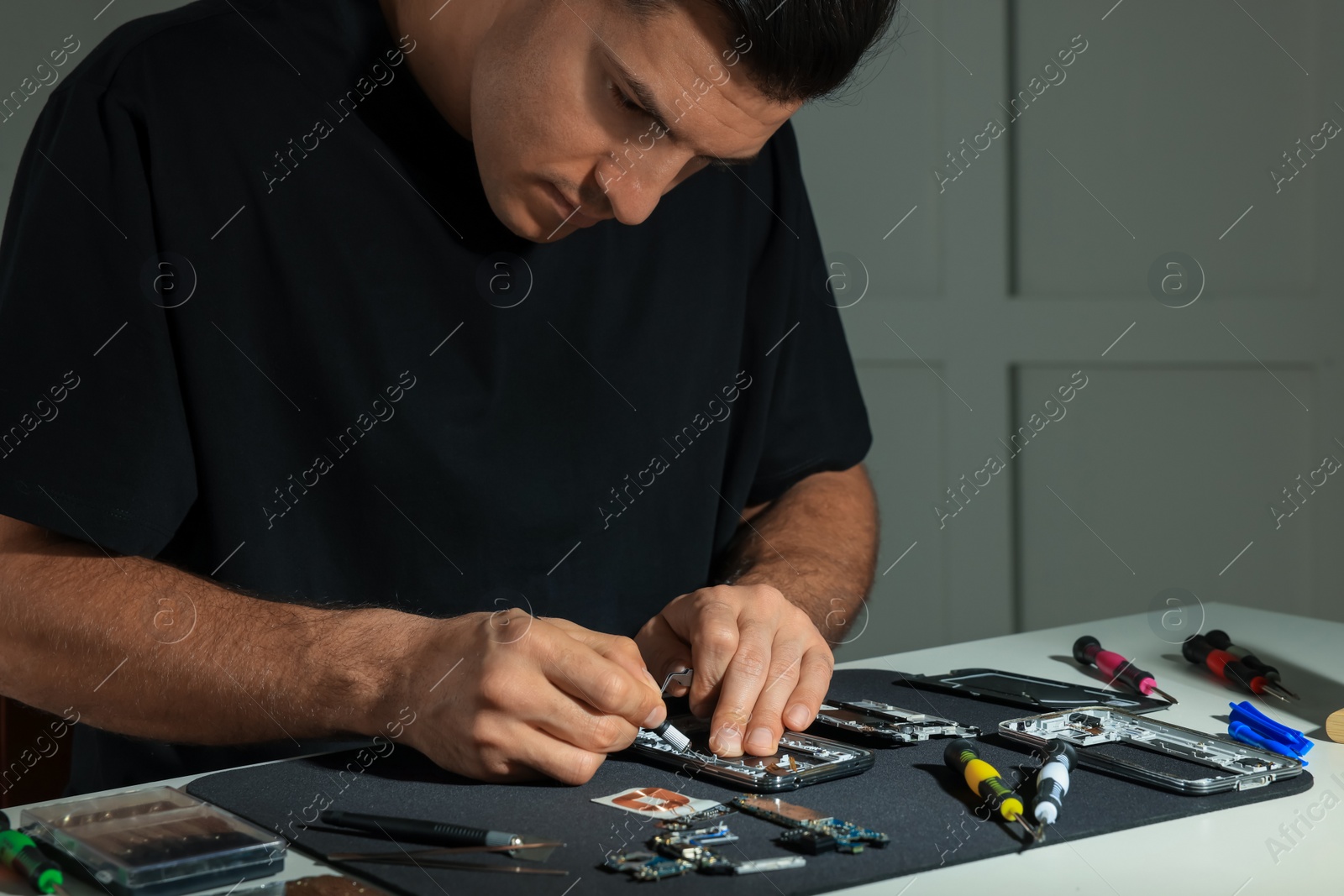 Photo of Technician repairing broken smartphone at table indoors, closeup