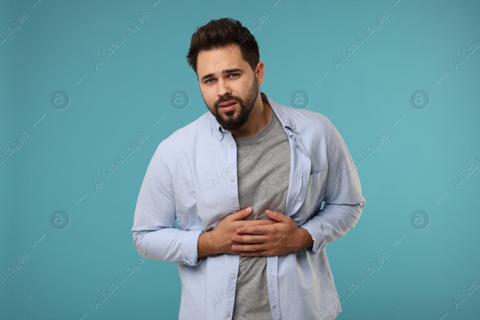 Photo of Young man suffering from stomach pain on light blue background