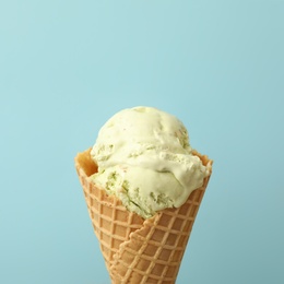 Photo of Delicious ice cream in waffle cone on light blue background, closeup