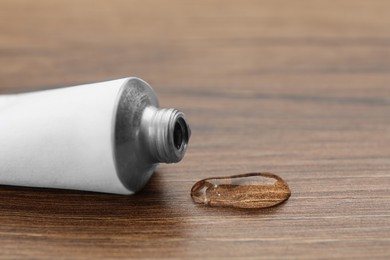 Photo of Open white tube with ointment on wooden table, closeup