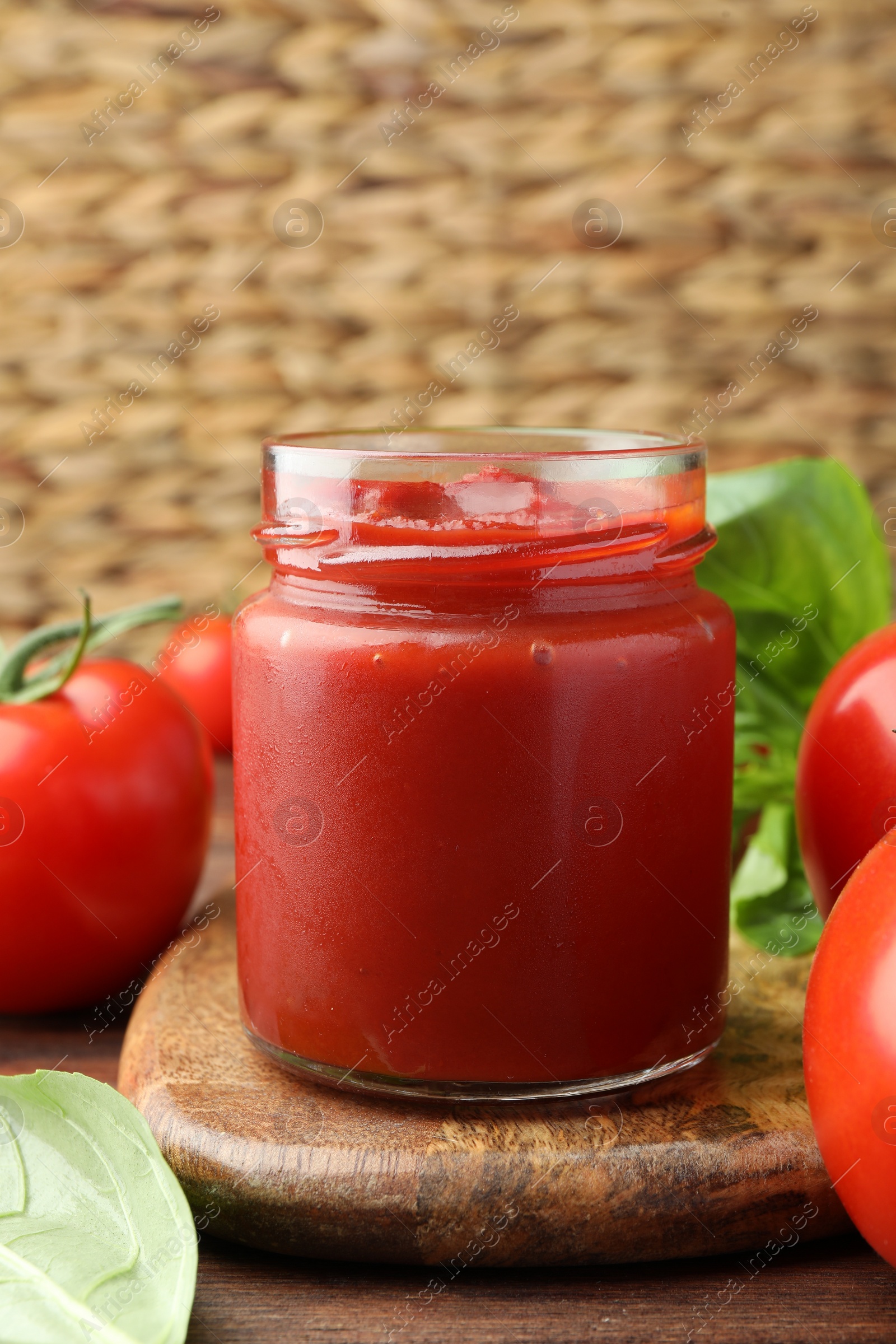 Photo of Jar of tasty ketchup and tomatoes on wooden table, closeup