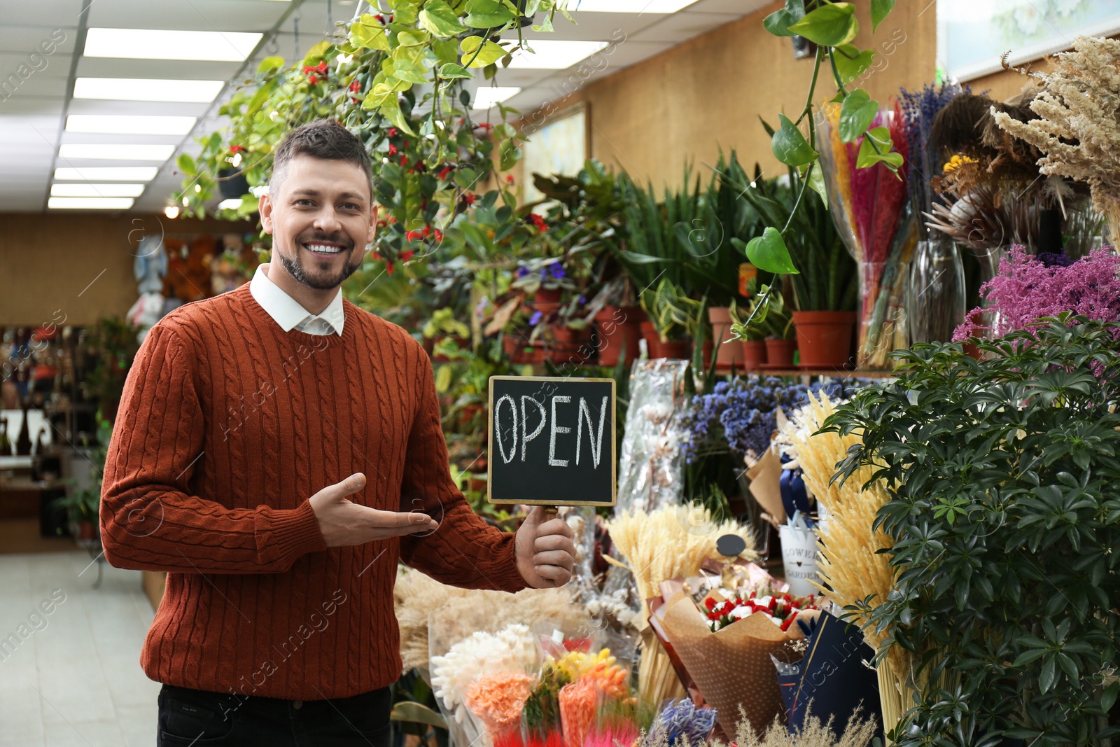 Photo of Male business owner holding OPEN sign in his flower shop